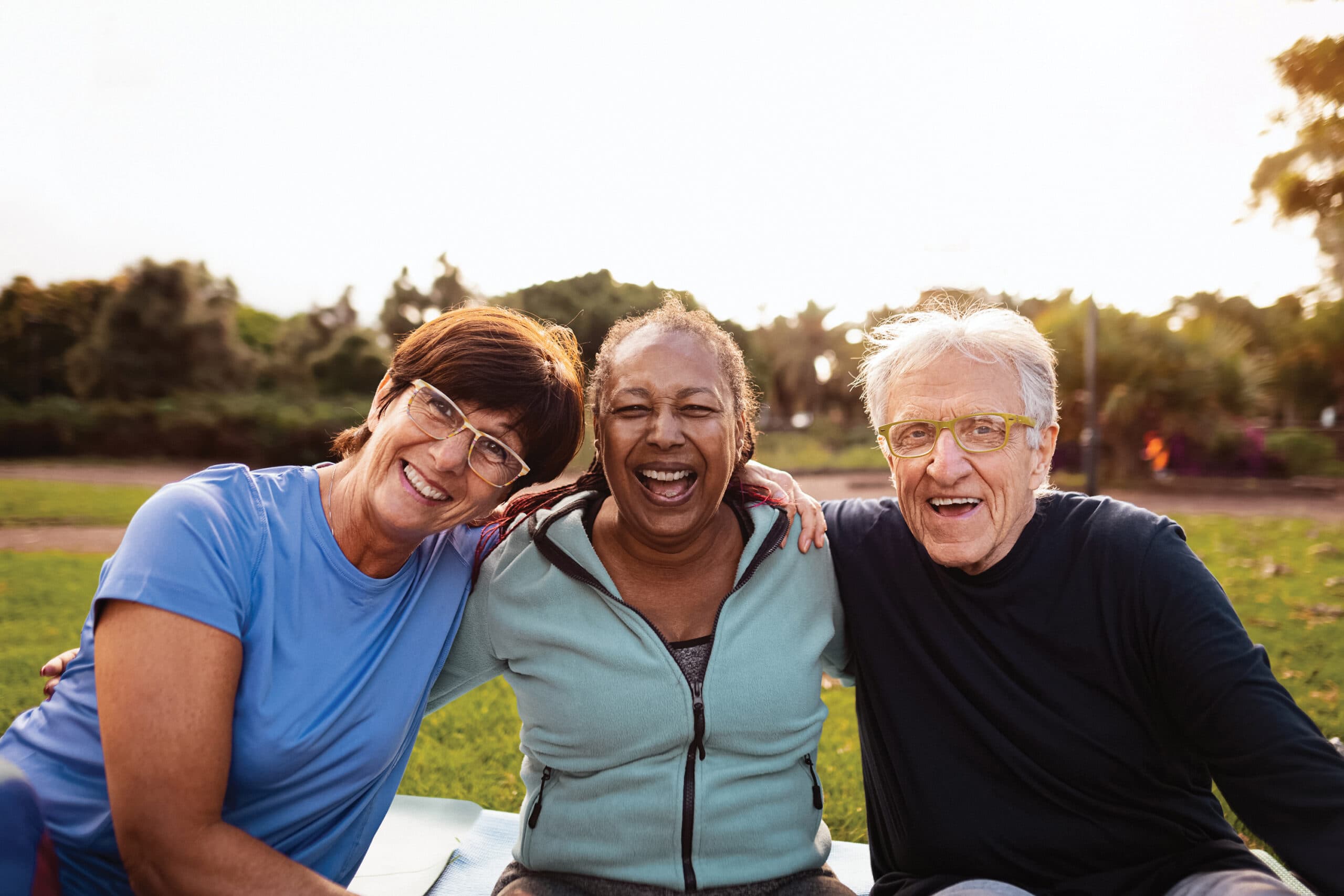 Three smiling friends sit on a blanket or mat outdoors