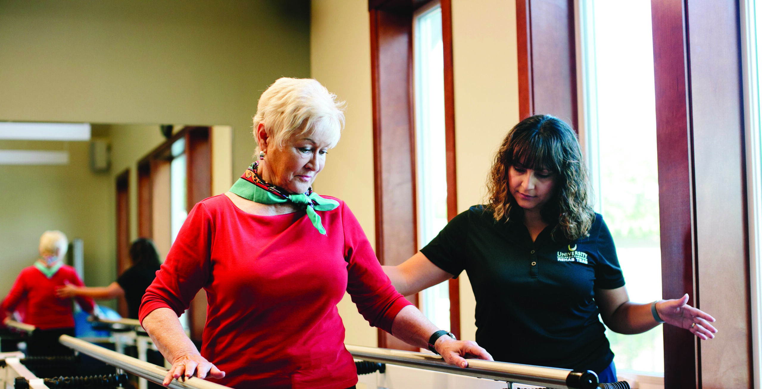 An older woman does a physical therapy exercise with a healthcare worker.